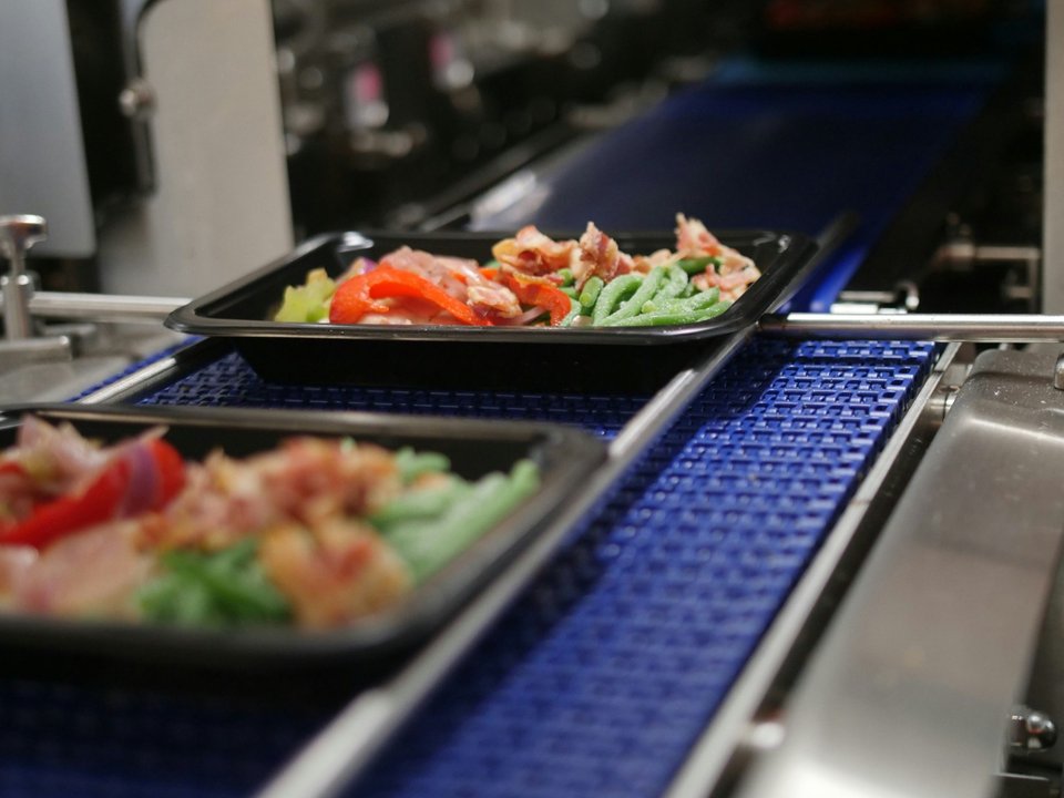 Trays of prepared vegetables and protein moving down a conveyor