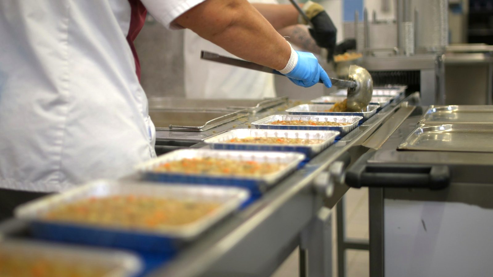 Gloved hands portioning food into trays on a production line