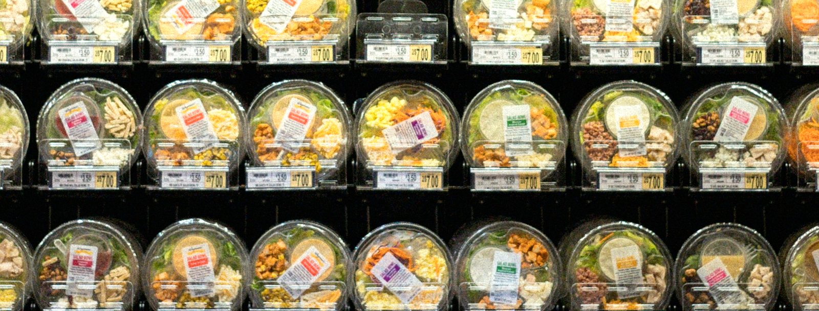 Rows of packaged, labeled salad bowls in a store cooler